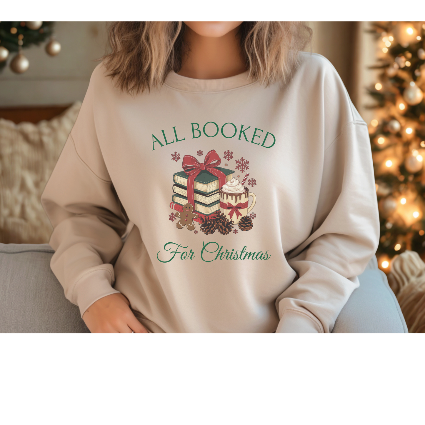 Person wearing a beige sweatshirt with Christmas-themed design and text, sitting in front of a decorated Christmas tree.
